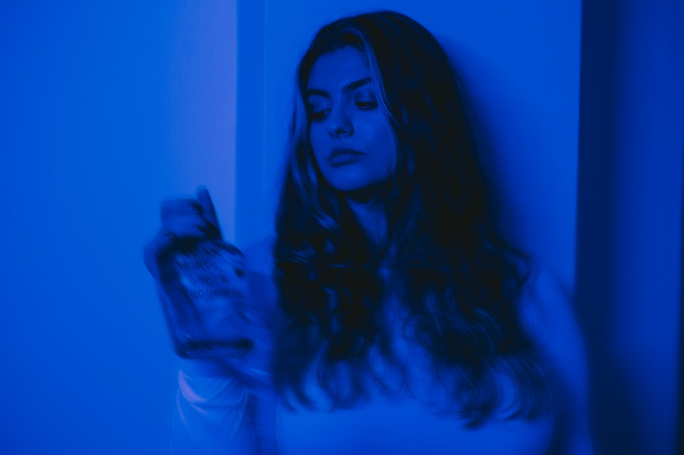 A girl washed in blue light holds a bottle of vodka